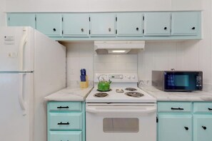 A kitchen with teal cabinets, a white refrigerator, a stove with a kettle, and a microwave.