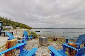 An outdoor seating area with blue Adirondack chairs and a metal fire pit, overlooking a body of water. - Stunning Soundfront Home in Coupeville with Private Beach Access and Fire Pit (Coupeville)
