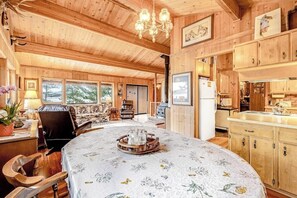 A wooden cabin interior with a dining area, kitchen, and living room.