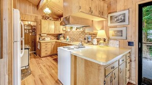 Ein Holzblockhaus-Interieur mit einer Küche, die eine zentrale Kochinsel, Holzausstattung und eine hängende Leuchte umfasst.