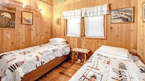 Ein Zimmer mit Holzwänden, zwei Betten, einem kleinen Tisch und gerahmten Bildern an den Wänden.