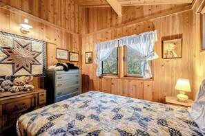 A wooden-paneled room with a bed, dresser, and a quilted wall hanging.