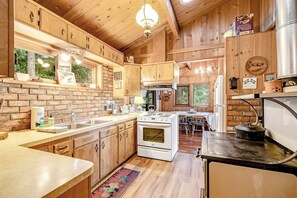 A wooden cabin kitchen with a brick backsplash, white appliances, and a dining area with a table and chairs.
