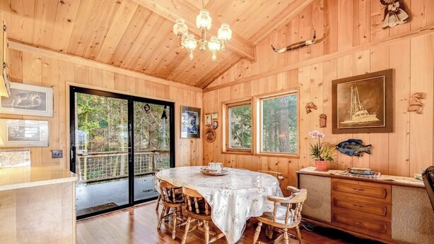 Ein Holzinterieur mit einem Esstisch, Stühlen, einer Kristallleuchtre und Blick durch Glastüren.
