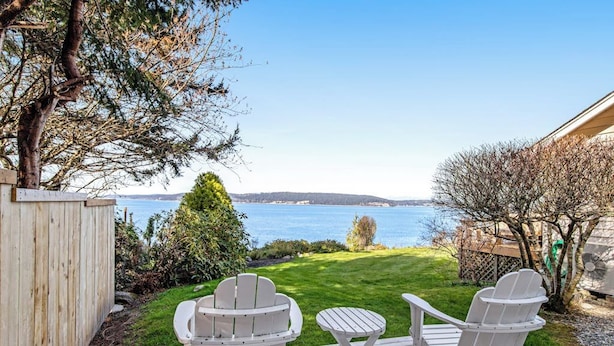 Una terraza con sillas Adirondack y una pequeña mesa con vista al agua.