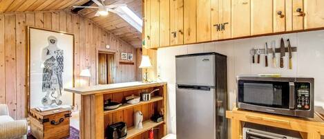 A compact kitchen with wooden cabinets, a stainless steel refrigerator, a microwave, and a toaster.