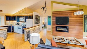 Een moderne keuken met een stenen achterwand, een eetgedeelte met een houten tafel, en een woonkamer met een open haard.