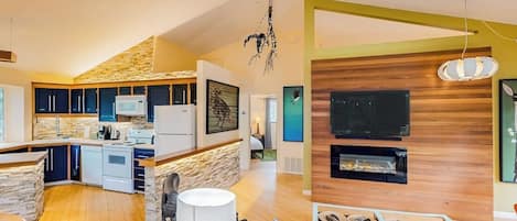 A modern kitchen with a stone backsplash, a dining area with a wooden table, and a living room with a fireplace.