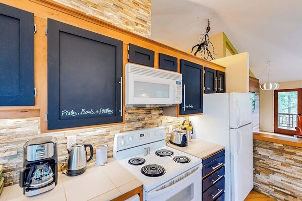A kitchen with a coffee maker, kettle, microwave, stove, and refrigerator. - Unique Treetop Home with 360 Degree Deck (Eastsound)