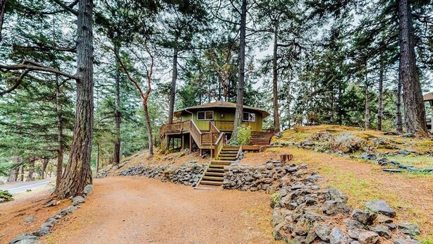 Een chalet met een houten trap naar een terras, omgeven door bomen en een onverhard pad.