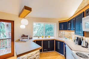 A modern kitchen with a stone accent wall, a large window, and a built-in stove. - Unique Treetop Home with 360 Degree Deck (Eastsound)