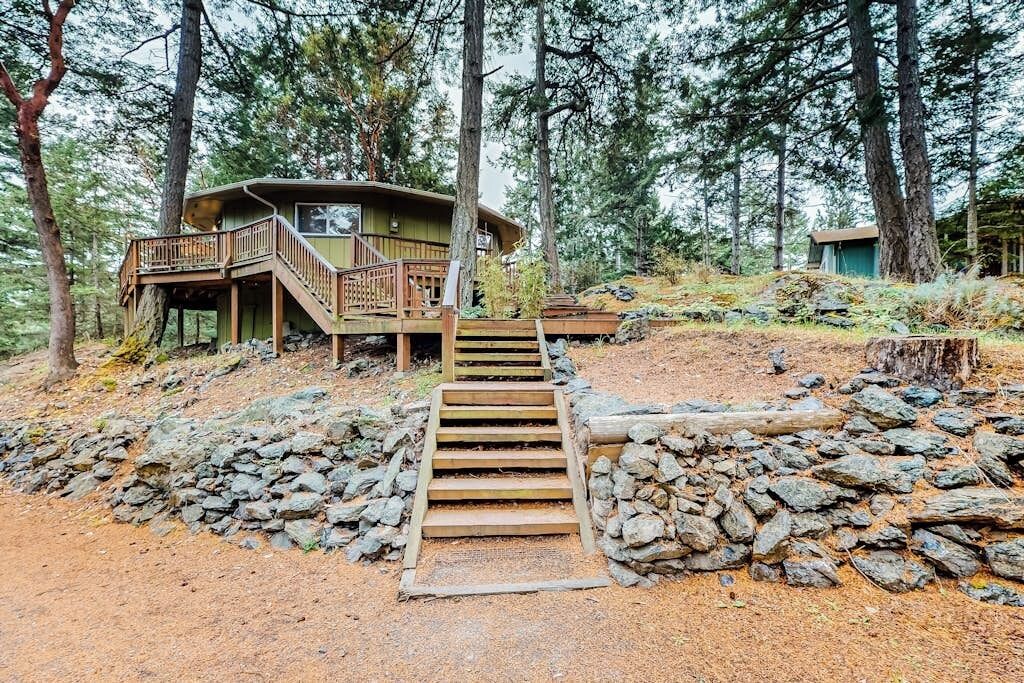 Una cabaña con una escalera de madera que conduce a una terraza, rodeada de un bosque.