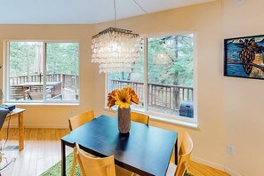 A dining area with a table, chairs, a vase with flowers, and a painting on the wall. - Unique Treetop Home with 360 Degree Deck (Eastsound)