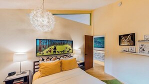 Een slaapkamer met een bed, nachtkastjes, een kroonluchter, kunstwerken en uitzicht op een balkon.