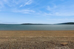Une plage de galets bordant un lac paisible, avec des collines qui se dessinent à l’horizon.