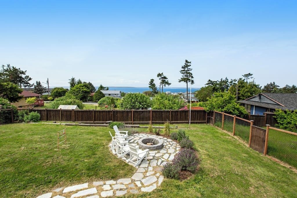 Patio trasero con un hogar de piedra, sillas blancas y una valla de madera.