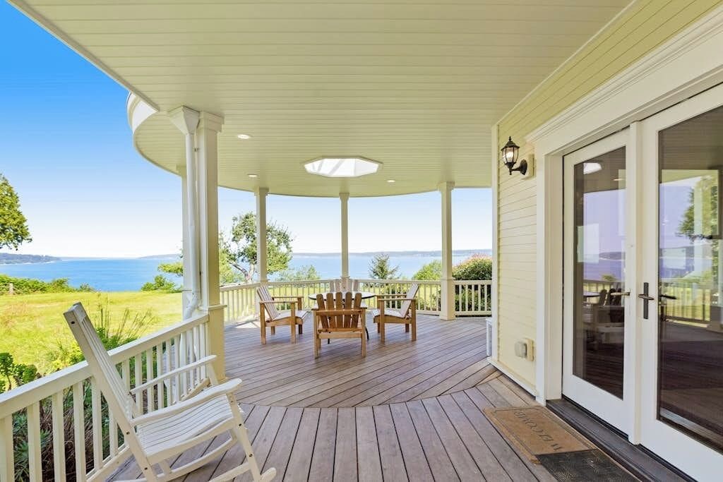 Eine überdachte Veranda mit Blick auf das Meer, Holzstühle und eine Tür mit Glasfenster.