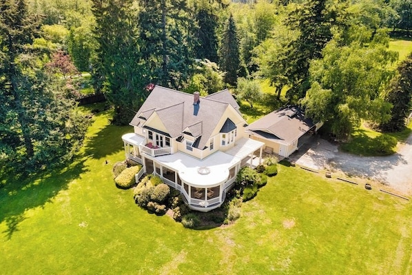 Une grande maison à deux étages, dotée d’une véranda qui fait le tour de la maison et d’un garage séparé.
