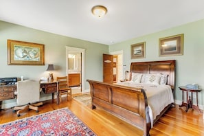 Une chambre à coucher avec un lit en bois, un bureau avec une chaise, un tapis et des œuvres d’art encadrées accrochées aux murs.