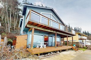 Kaksikerroksinen talo, jossa on puinen terassi ja katettu ulkotila oleskelua varten.