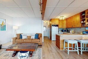 Ein Wohnzimmer mit einer Couch, einem Couchtisch und einer Küchenzeile mit Holzschränken und einer Mikrowelle.