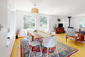 A modern living room with a dining area, large windows, a fireplace, and a television. - Relaxing Coupeville Home with Water Views, Fire Pit, and Beach Access (Coupeville)
