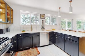 Een moderne keuken met donkere kasten, witte aanrechtbladen en een groot raam dat voor natuurlijk licht zorgt.