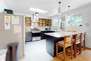 A modern kitchen with a central island, wooden chairs, and a view of the outdoors. - Relaxing Coupeville Home with Water Views, Fire Pit, and Beach Access (Coupeville)