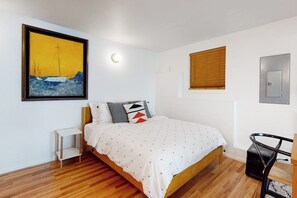 A bedroom with a bed, a bedside table, a wall-mounted light, a window with blinds, and a door. - Relaxing Coupeville Home with Water Views, Fire Pit, and Beach Access (Coupeville)