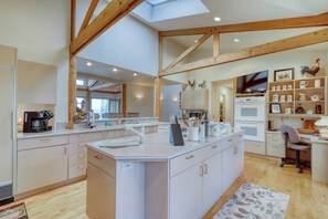 A modern kitchen with a central island, wooden beams, a skylight, and a dining area with a chair.