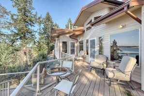 A deck with outdoor furniture, a glass balustrade, and a view of the surrounding forest.