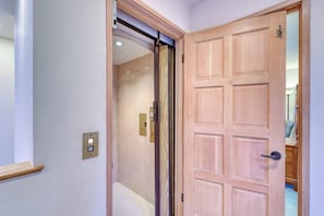 Un pasillo con una puerta de madera, una puerta corredera de vidrio y un interruptor de luz en la pared.