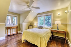 Ein Schlafzimmer mit einem Bett, einem Nachttisch, einem Schreibtisch, einem Deckenventilator und zwei Fenstern.