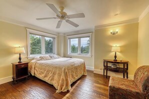 A bedroom with a bed, two nightstands, a chair, a ceiling fan, and large windows. - Welcoming 5 Bedroom Orcas Island Home with Stunning Bay Views and Modern Amenities (Eastsound)
