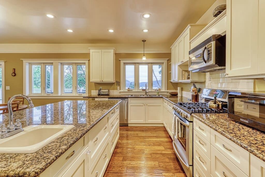 Una cocina con encimeras de granito, armarios blancos, una estufa de acero inoxidable y una ventana con vistas al paisaje.