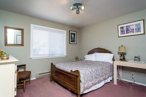 Une chambre à coucher avec un lit en bois, un bureau, une chaise, une fenêtre avec des stores et un luminaire au plafond.