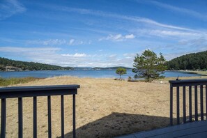 A deck overlooking a lake with a clear sky and distant hills. - Modern Waterfront House on Lopez Island with Beach Access and Stunning Views (Lopez Island)