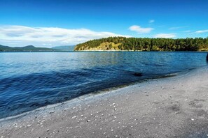 A beach with clear water, a sandy shore, and a forested island in the distance. - Modern Waterfront House on Lopez Island with Beach Access and Stunning Views (Lopez Island)