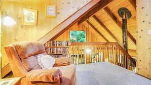 A cozy room with a sloped ceiling, a wooden staircase, a comfortable sofa, and a bookshelf. - Quiet 2 BR Lopez Island Cabin Near Beach (Lopez Island)