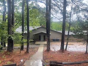 A two-story building with a covered porch, surrounded by tall trees and a wet ground, likely after rain. - Paradise in the woods 
Spacious 5-bedroom cabin in serene Oxford with AC (Oxford)