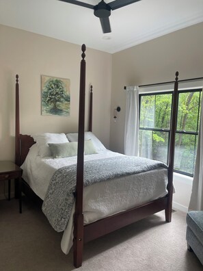 Una cama con dosel y columnas, una mesita de noche y una ventana con vistas a árboles.