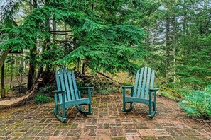 Zwei Adirondack-Stühle auf einem Ziegelweg, umgeben von dichtem Grün.