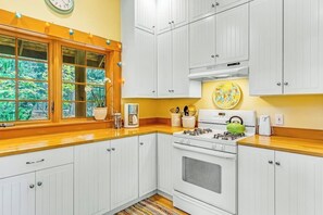 A kitchen with white cabinets, a stove, and a window with a view of greenery.