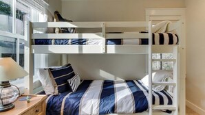 Ein Stockbett mit gestreifter Bettdecke, ein Nachttisch mit Lampe und ein Fenster mit Jalousien.