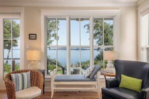 A room with a bench, two chairs, and a view of a lake.