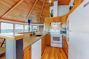 Une cuisine moderne avec des meubles en bois, un four encastré et une vue sur la mer grâce à de grandes fenêtres.