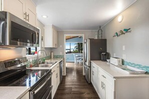A modern kitchen with stainless steel appliances, a tiled backsplash, and a view to the outside. - Scenic Log Cabin with Hot Tub, Beach Access and Game Room (Freeland)