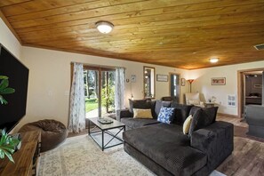 A living room with a wooden ceiling, a sofa set, a coffee table, and a television. - Scenic Log Cabin with Hot Tub, Beach Access and Game Room (Freeland)