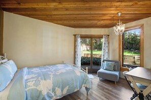 A bedroom with a bed, a grey sofa, a table, and a chandelier. - Scenic Log Cabin with Hot Tub, Beach Access and Game Room (Freeland)
