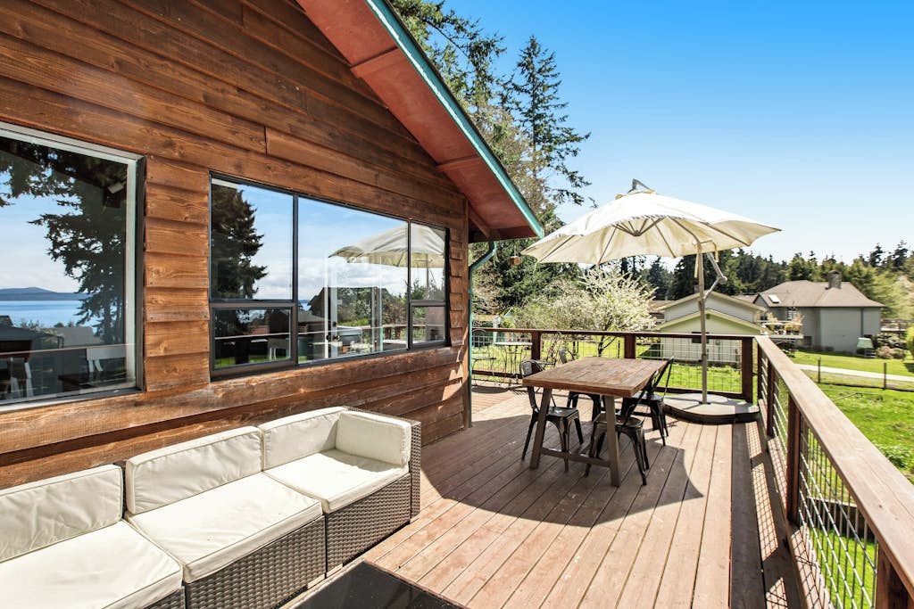 A wooden deck with a table and chairs, a cushioned bench, and a view of the surrounding landscape.